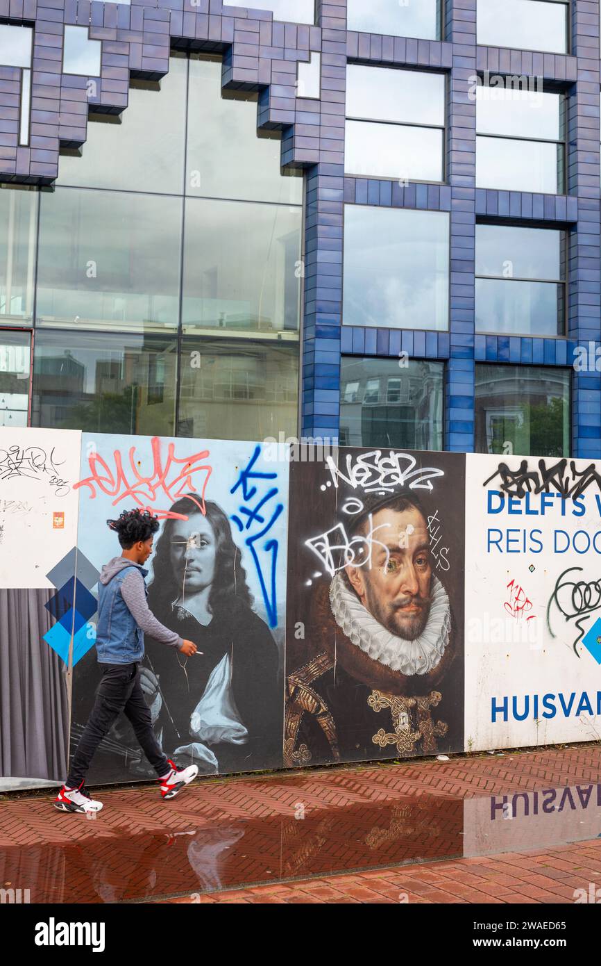 Homme marchant passant devant des peintures murales lors de la nouvelle construction d'un bâtiment multifonctionnel appelé « huis van Delft » aux couleurs de delftware dans le centre-ville de Delft Banque D'Images