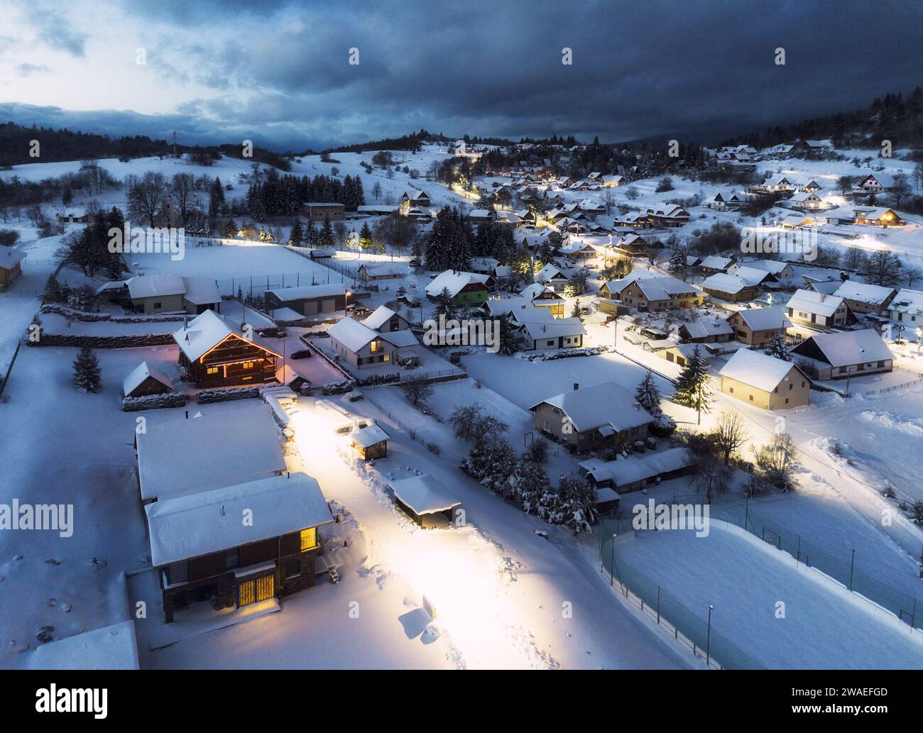 Vue sur la chaîne de montagnes enneigées et le village avec des maisons illuminées situées au bas de la colline en Slovaquie au coucher du soleil Banque D'Images
