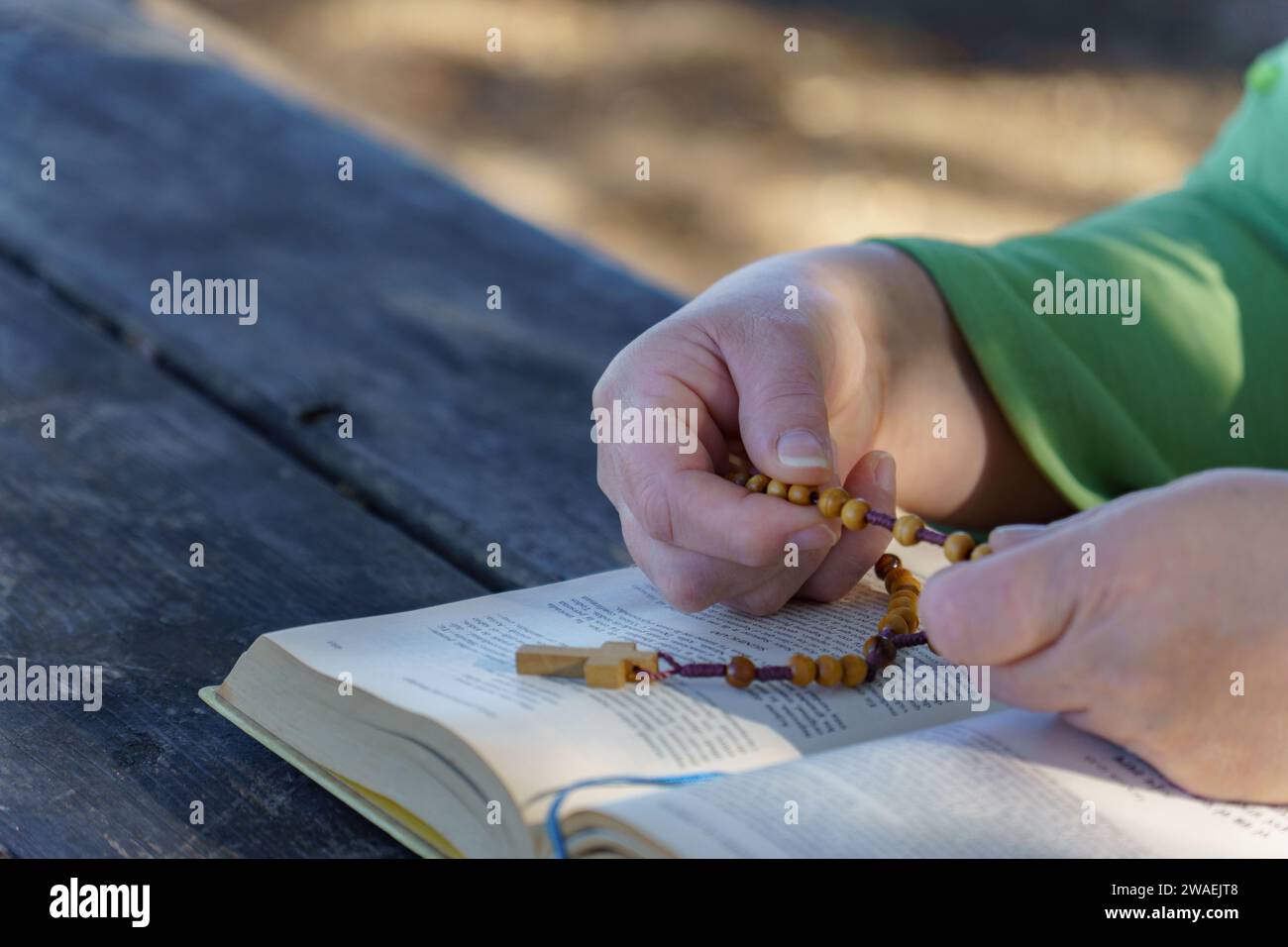 des mains d'une femme priant les perles du chapelet sur une bible dans la campagne ensoleillée Banque D'Images