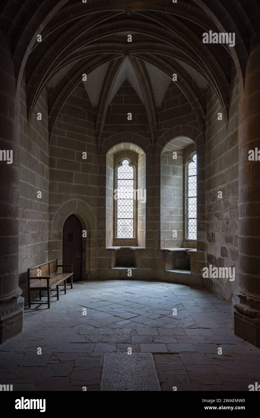 Détail d'une petite pièce dans l'abbaye du Mont Saint Michelle, fenêtres et haut plafond, dôme, porte en bois et un banc en bois, il fait sombre Banque D'Images