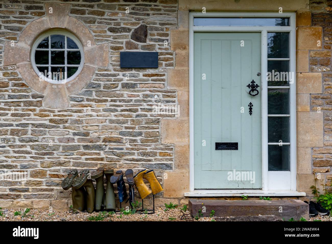 Entrée d'Un Cottage avec des bottes en caoutchouc de différentes tailles sous la porte en Angleterre Banque D'Images