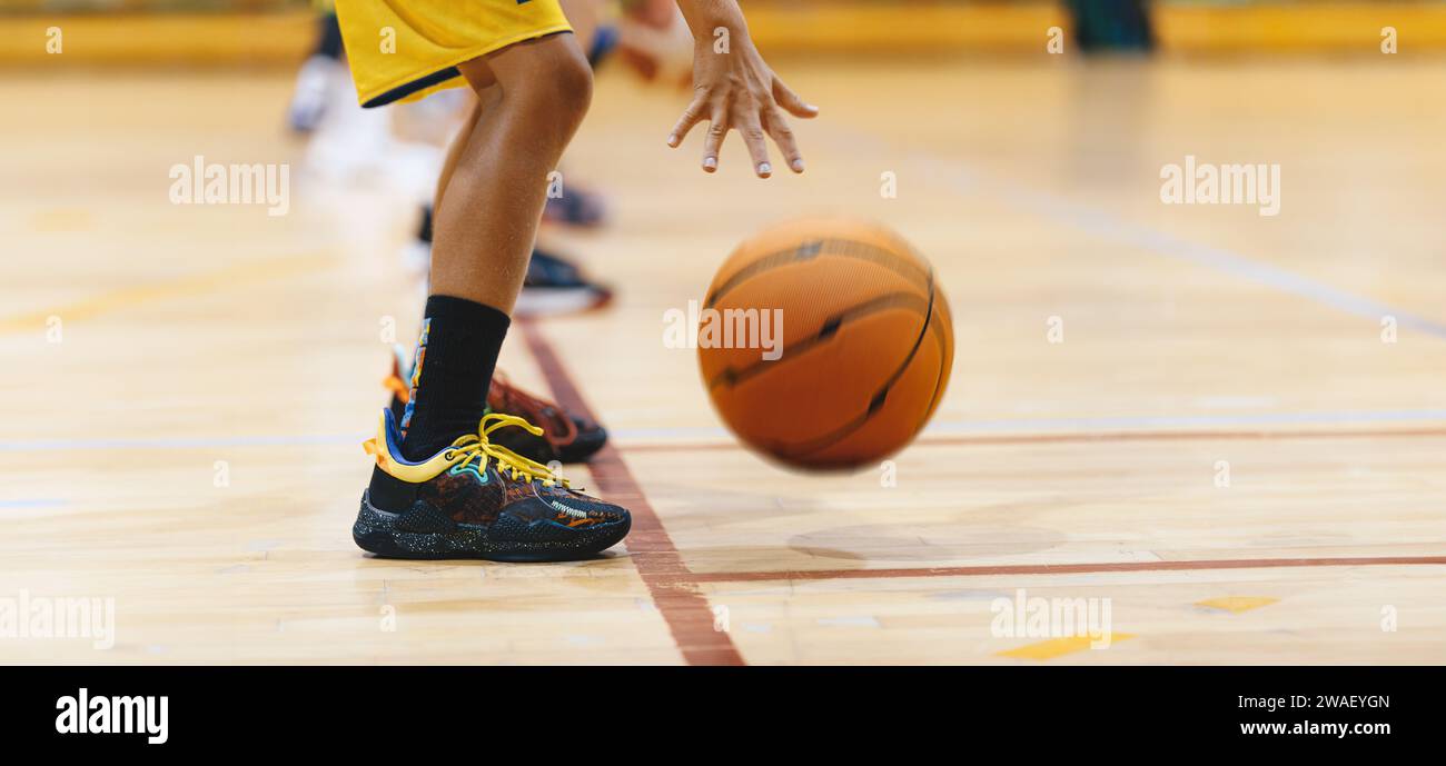 Image horizontale d'un jeune joueur de basket-ball faisant rebondir la balle dans l'exercice d'entraînement. Équipe de basketball de jeunes à l'entraînement. Séance d'entraînement de basket-ball pour l'école Banque D'Images