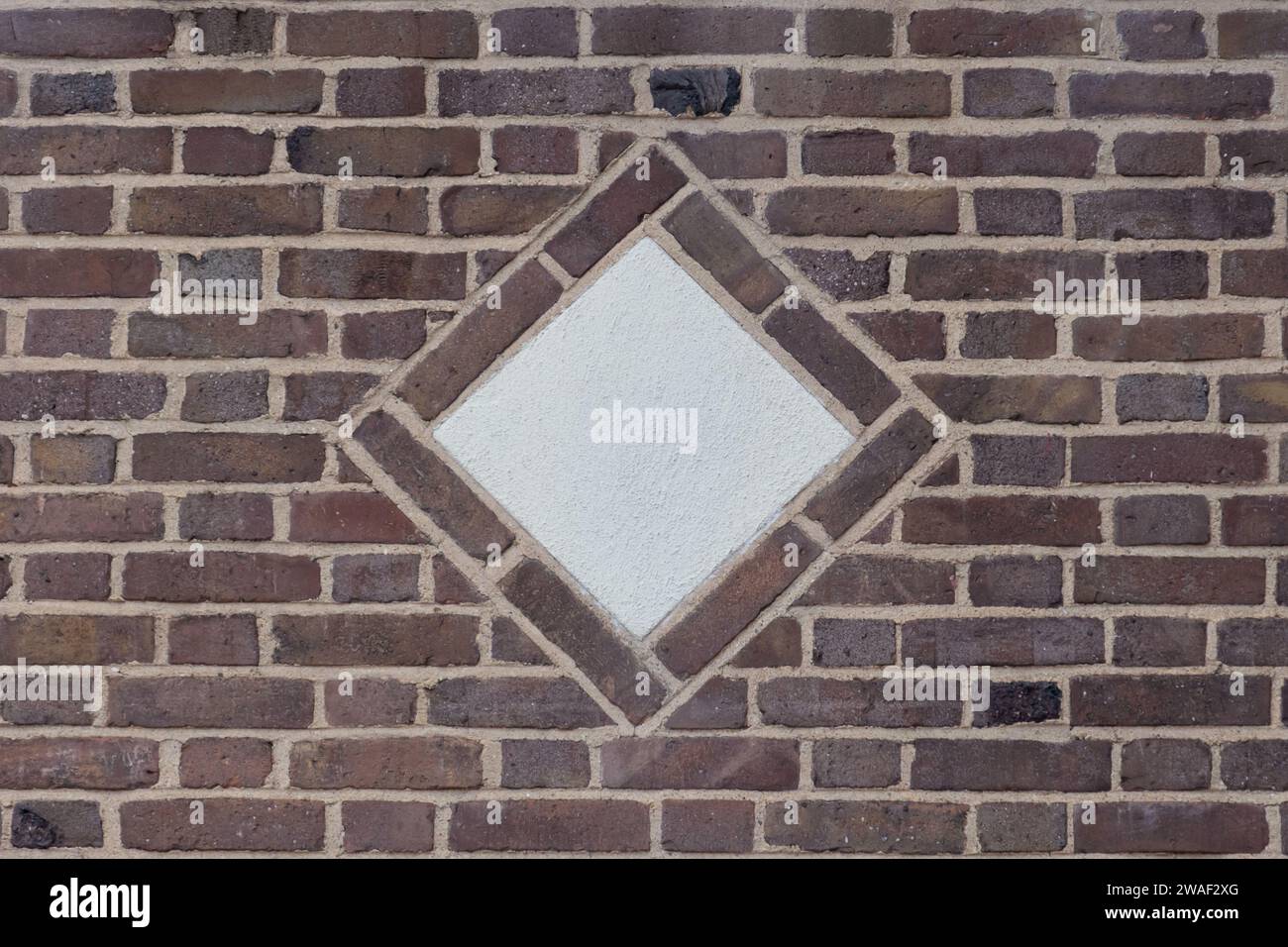 un médaillon décoratif en forme de diamant en béton au centre d'un mur de briques brunes rustiques en motif de briquetage de lien flamand, espace de copie Banque D'Images