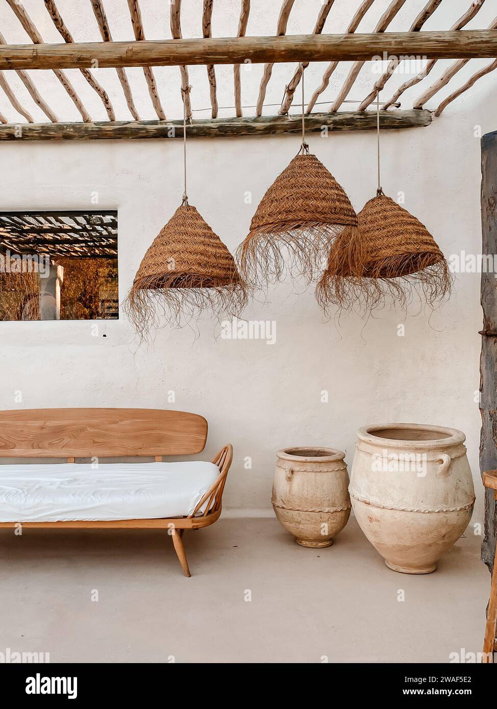 Cette image présente un intérieur confortable et rustique avec un banc en bois, des récipients en argile et des lampes en rotin Banque D'Images