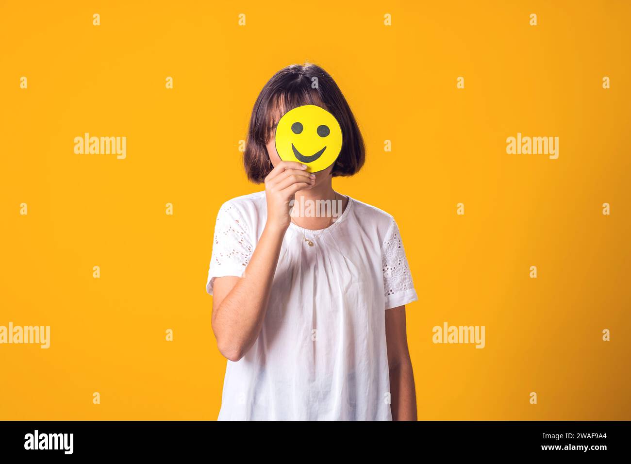 Fille tient des émoticônes heureuses dans le friont de visage. Santé mentale, psychologie et concepts émotionnels de l'enfant Banque D'Images