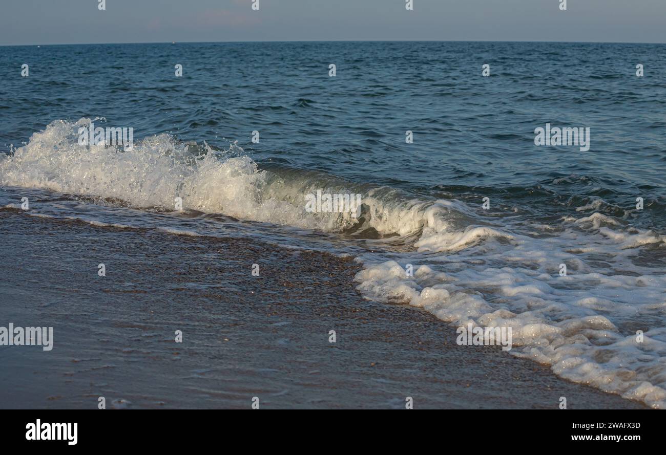 Une grande et forte onde de tempête de couleur turquoise avec des éclaboussures de mousse blanche coule et se brise sur le rivage. Banque D'Images