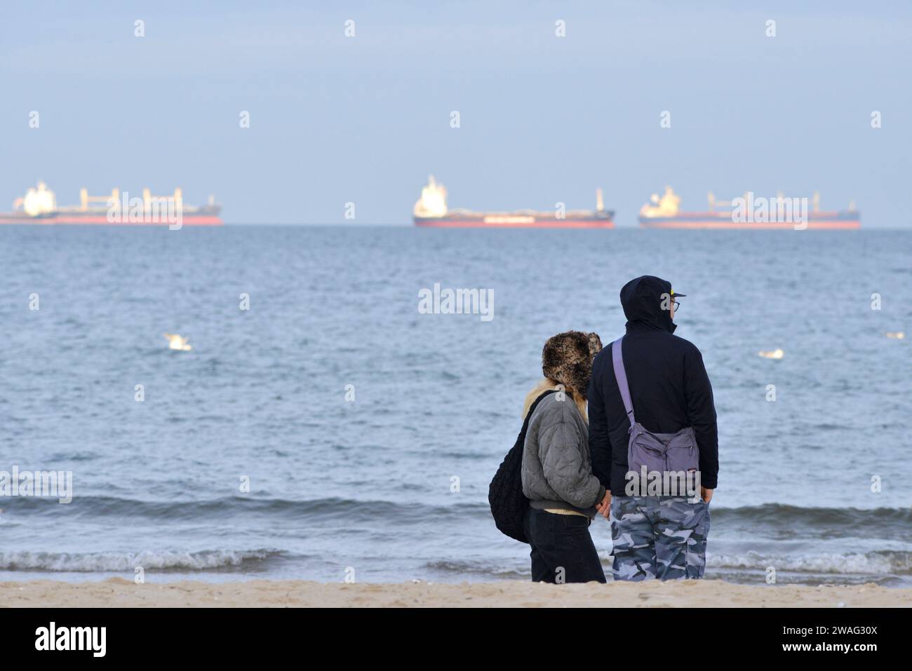 Couple avec des vestes à la plage de Gdansk regarder les navires-citernes dans la baie de Gdansk, la mer Baltique, Gdansk, Pologne, Europe, UE Banque D'Images