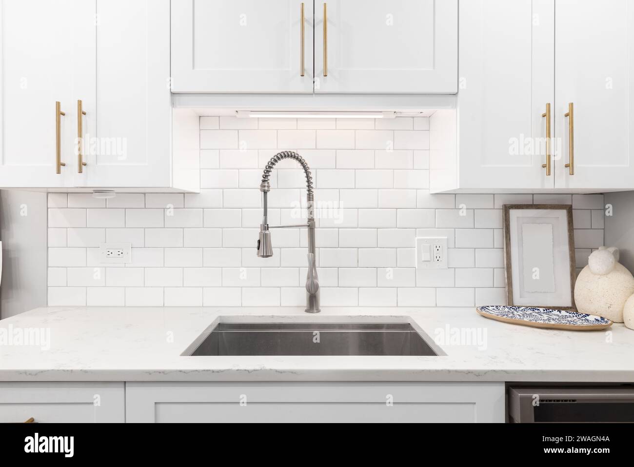 Un détail de robinet de cuisine avec des armoires blanches, de la quincaillerie dorée et un dosseret de tuile de métro. Banque D'Images