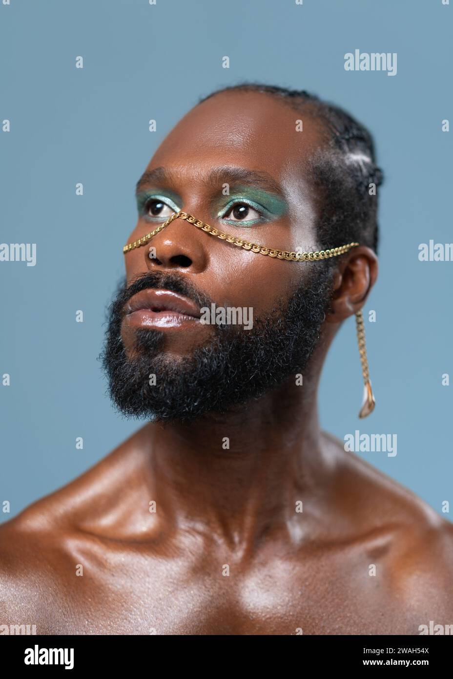 Homme gay afro-américain confiant barbu avec maquillage lumineux isolé sur fond bleu, Close up portrait. Respire le sens de la fierté et de l'individualité. Pouvoir de diversité du style personnel. Banque D'Images