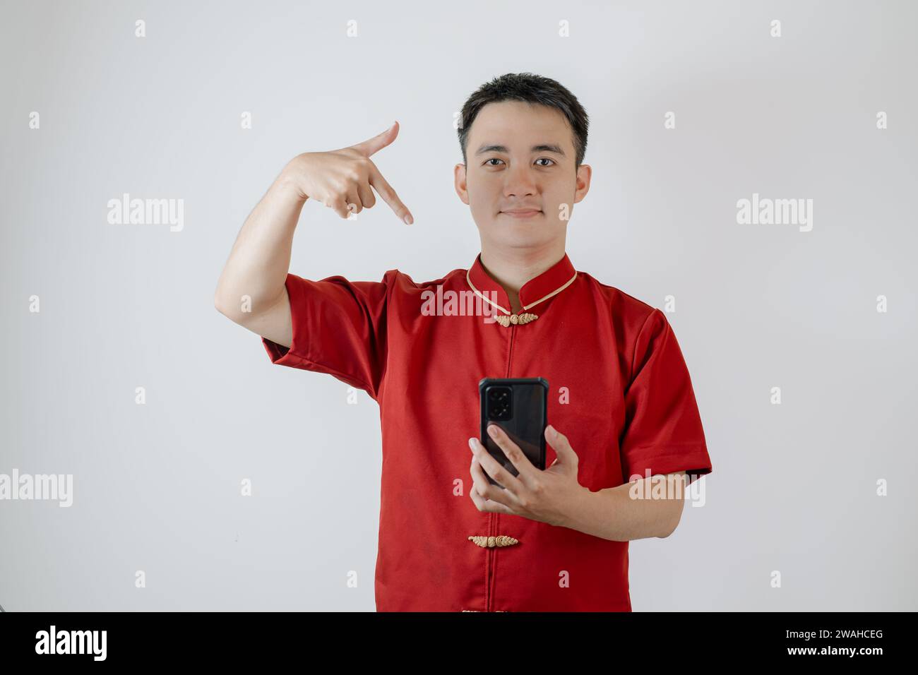 Homme asiatique portant un tissu traditionnel chinois ou Cheongsam pointant son smartphone sur fond blanc Banque D'Images