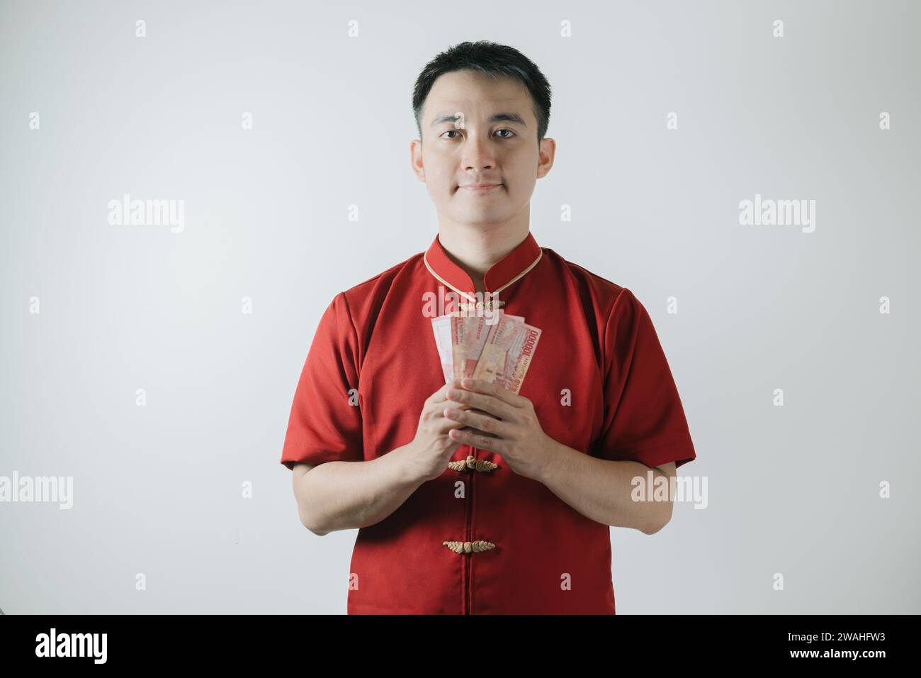 Homme asiatique portant Cheongsam ou tissu traditionnel chinois tient des sommes d'argent et regarde la caméra sur fond blanc Banque D'Images