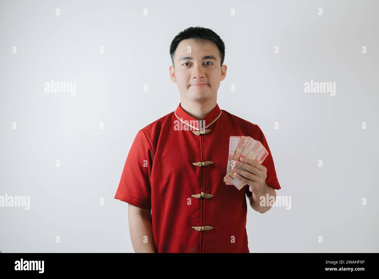 Homme asiatique portant Cheongsam ou tissu traditionnel chinois tient des sommes d'argent et regarde la caméra sur fond blanc Banque D'Images