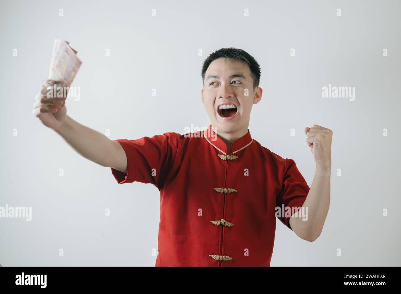 Expression de visage excité de l'homme asiatique portant Cheongsam ou tissu traditionnel chinois tout en tenant des montants d'argent sur fond blanc Banque D'Images