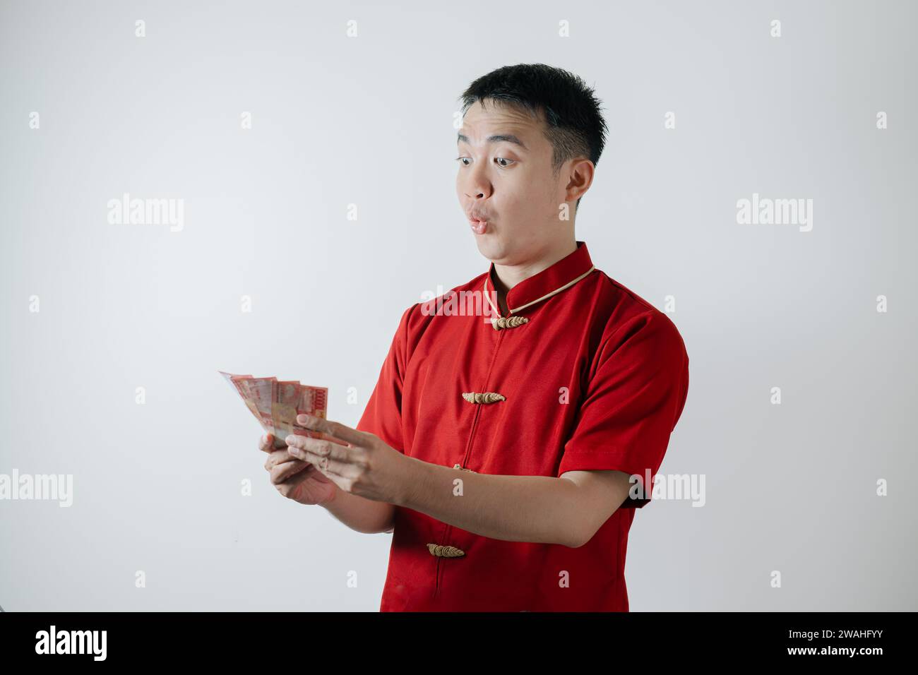 Visage surpris de l'homme asiatique portant Cheongsam ou tissu traditionnel chinois tient des montants d'argent sur fond blanc Banque D'Images