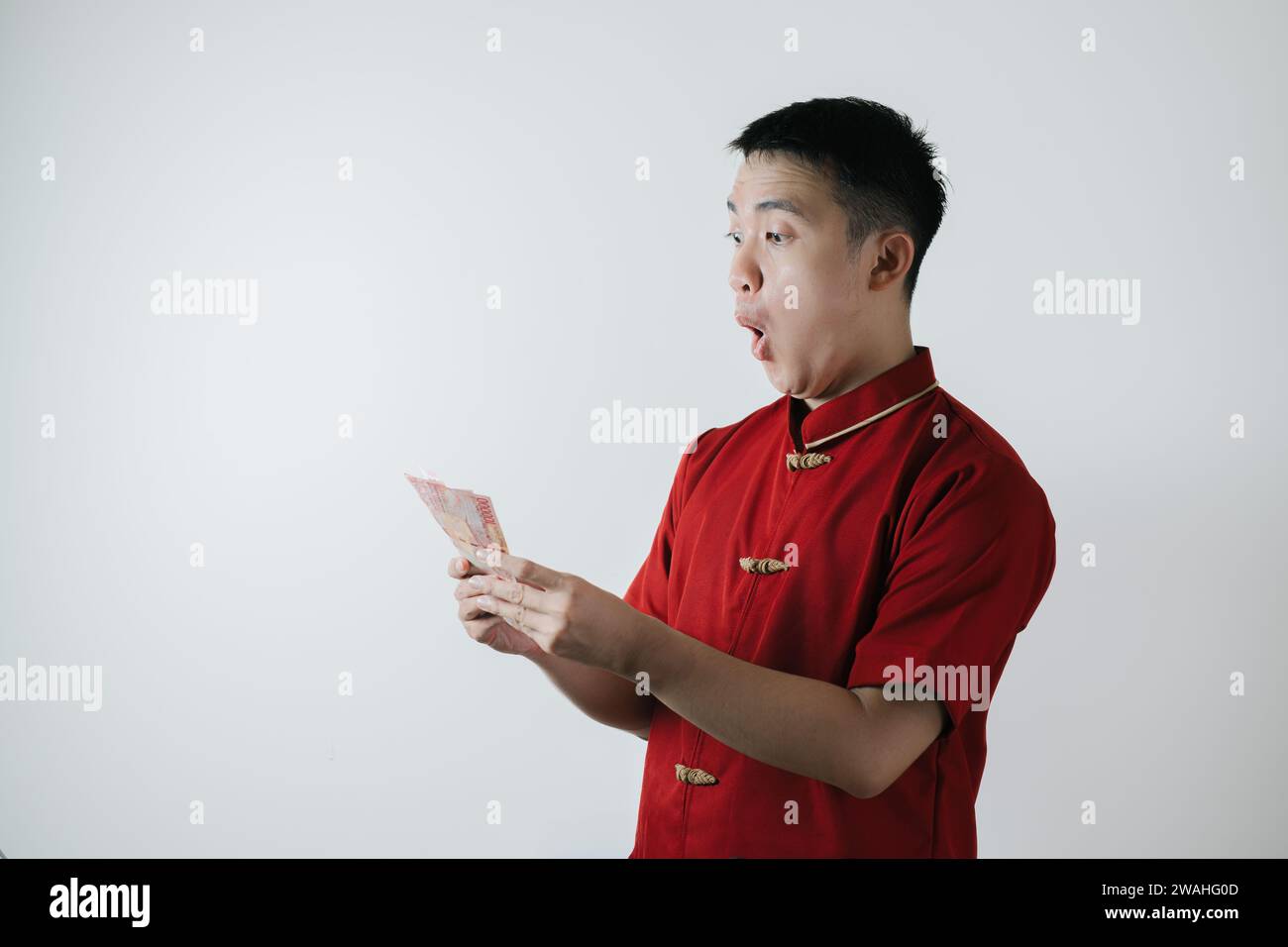 Visage surpris de l'homme asiatique portant Cheongsam ou tissu traditionnel chinois tient des montants d'argent sur fond blanc Banque D'Images