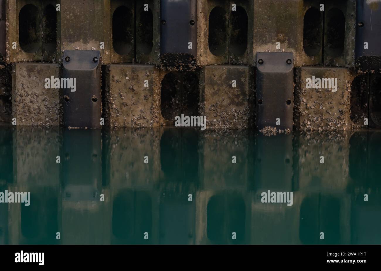 Bloc de béton et mur d'acier et reflet dans l'eau verdâtre Banque D'Images