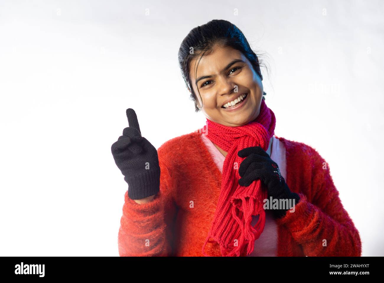 Une belle femme indienne en vêtements d'hiver rouge souriant et pointant sur fond blanc Banque D'Images