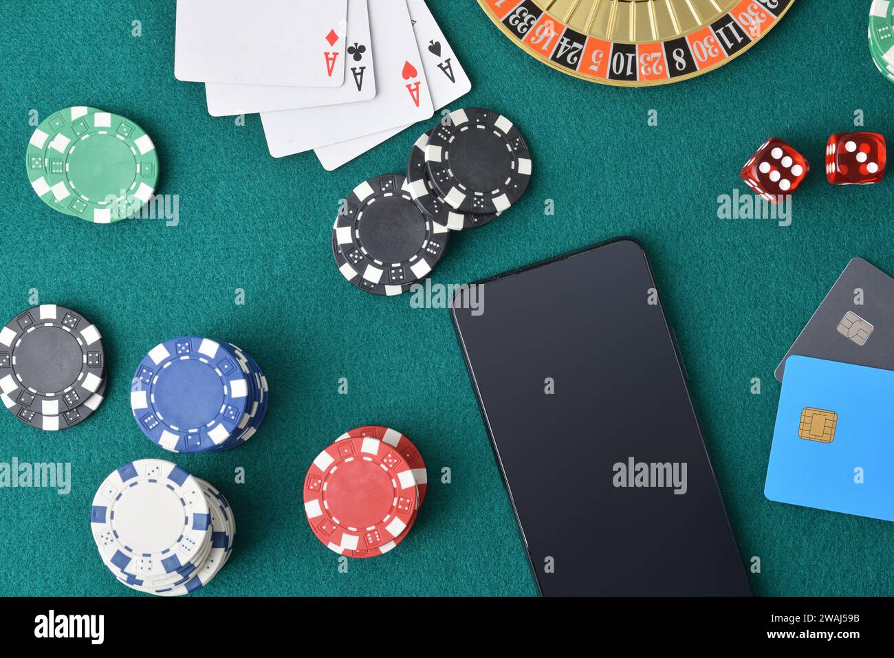 Concept de jouer à des jeux de casino en ligne avec smartphone sur une table de jeu avec feutre vert plein d'objets de jeu et de cartes bancaires. Vue de dessus. Banque D'Images