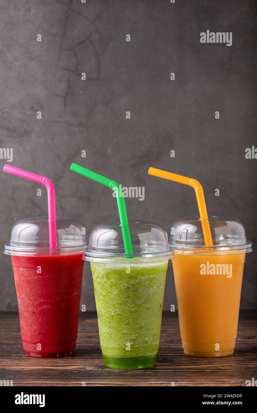 Trois smoothies de fruits différents dans des verres à emporter en plastique sur fond en bois Banque D'Images