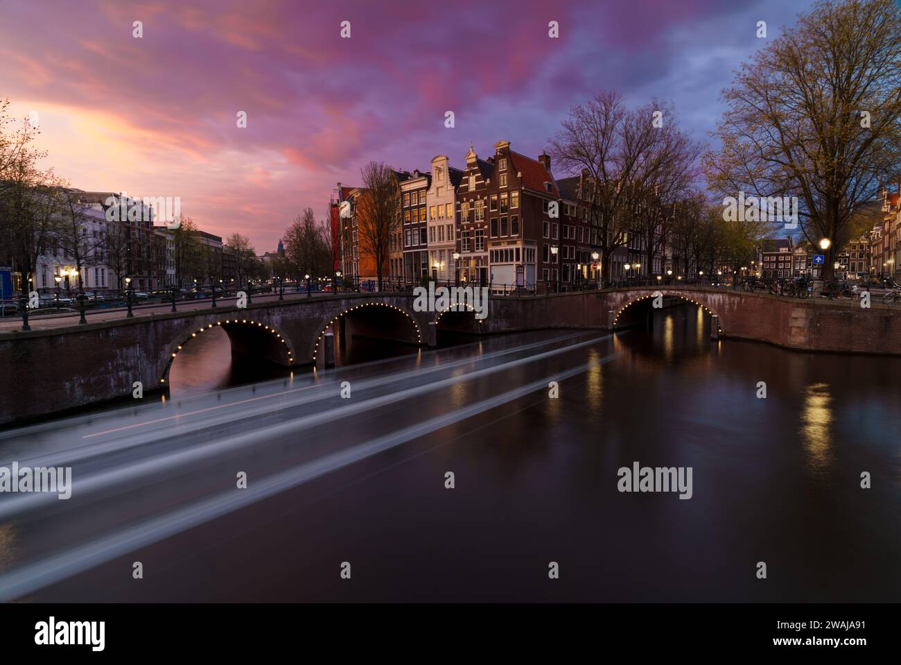Le crépuscule se colore sur les canaux d'Amsterdam avec des ponts historiques et des maisons sous un ciel de coucher de soleil vibrant Banque D'Images
