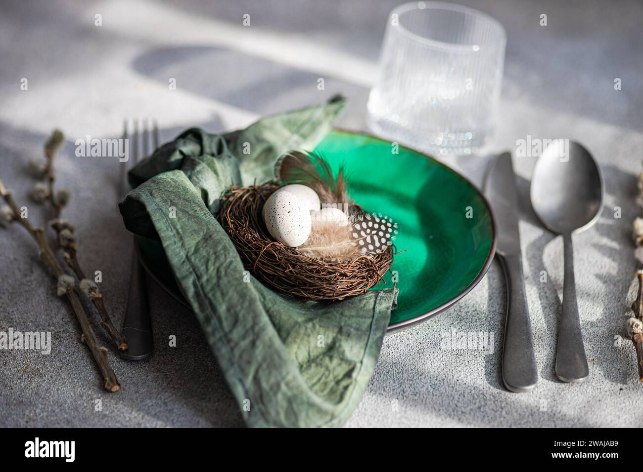 Angle élevé de la table de Pâques, présentant une assiette en céramique verte vibrante avec un petit nid avec des œufs tachetés et des plumes, placé sur une surface grise Banque D'Images