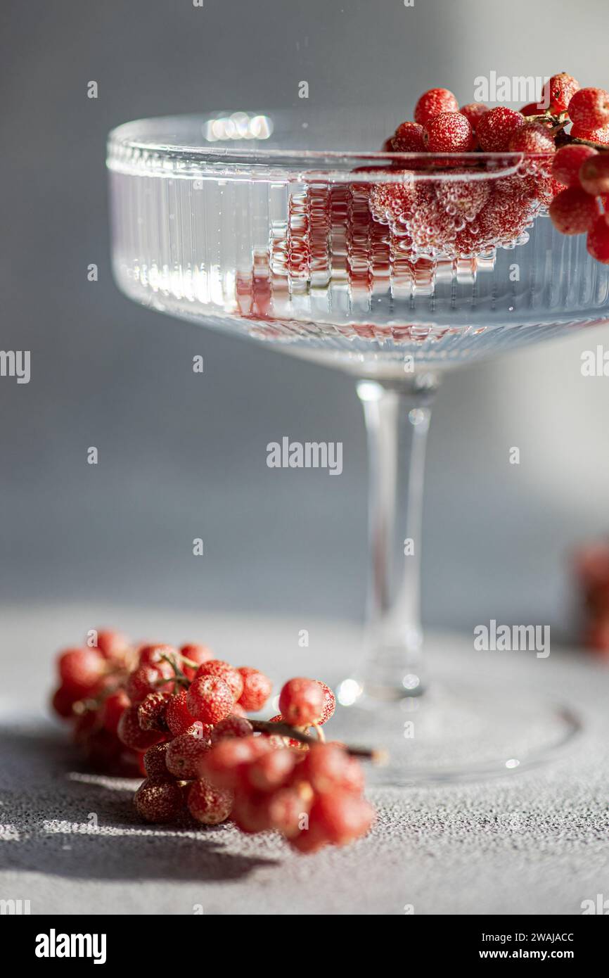 Un verre sophistiqué déborde d'eau et de délicates baies rouges, posé sur un fond doux et léger Banque D'Images