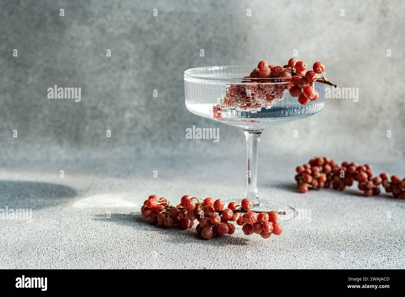 Un élégant verre à cocktail rempli de vin perché sur un fond gris texturé, entouré de grappes éparpillées de raisins rouges Banque D'Images