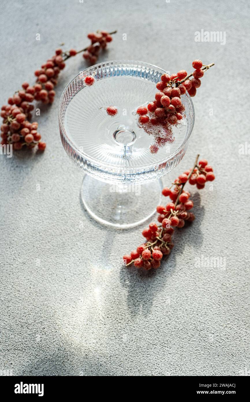 Un support de gâteau en verre transparent sur une surface texturée, orné de petites baies rouges éparpillées autour Banque D'Images