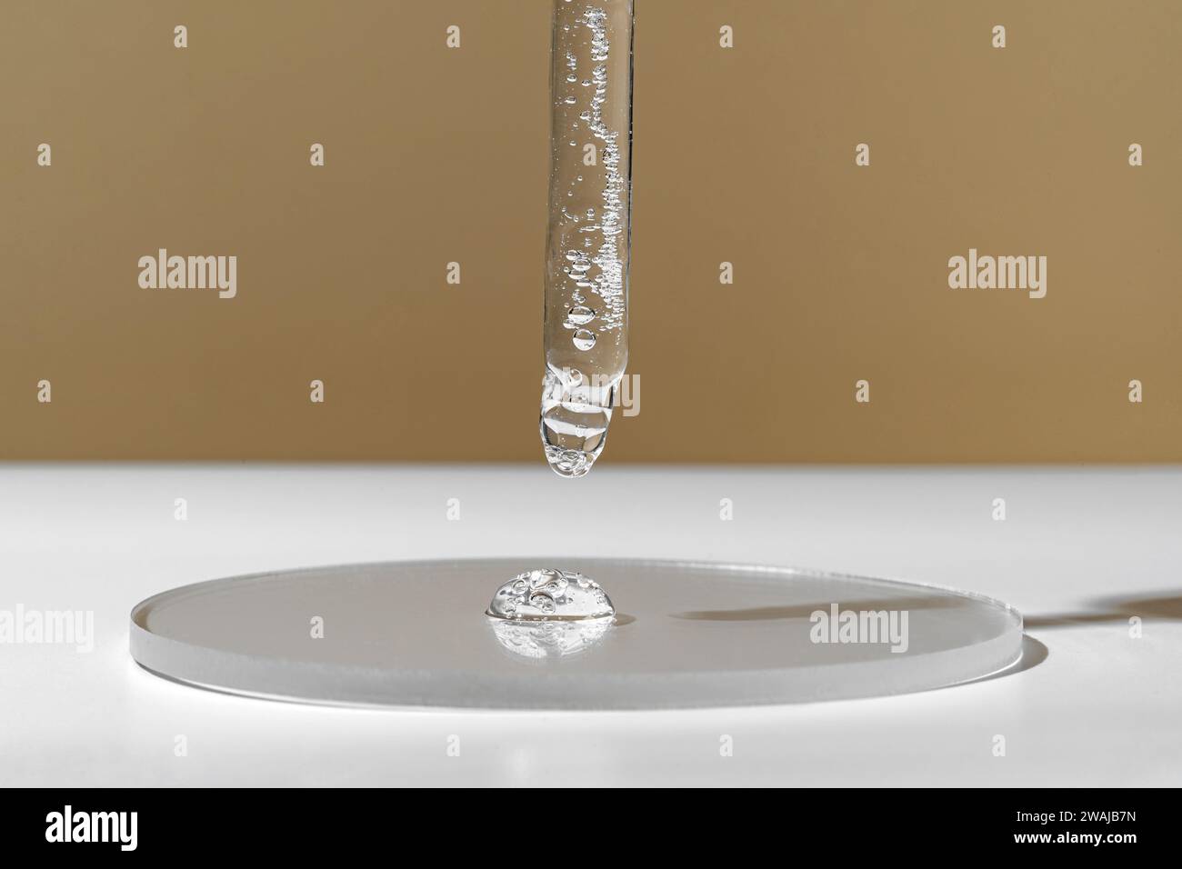 Un compte-gouttes précis libère une seule goutte de liquide clair sur une surface en verre sur un fond neutre incarnant la pureté et la précision dans les soins de la peau Banque D'Images