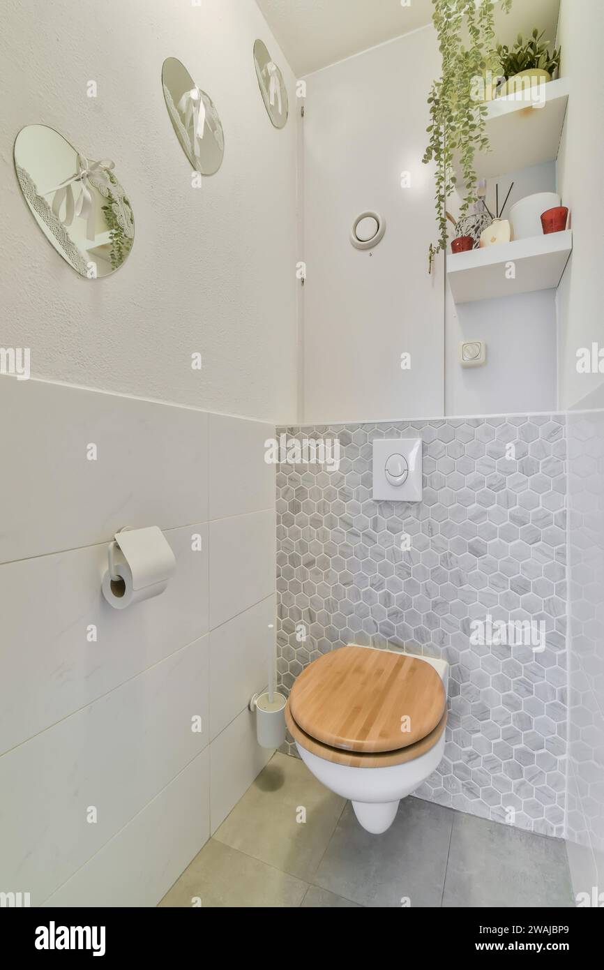 Siège de toilette en bois avec décors sur mur blanc et étagères dans une petite salle de bains carrelée à l'appartement contemporain Banque D'Images