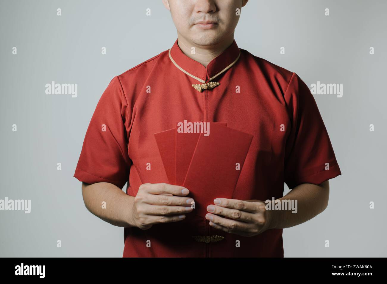 Homme asiatique portant Cheongsam ou tissu traditionnel chinois tient angpao ou cadeau monétaire rouge sur fond blanc. Gong Xi Fa Cai. Banque D'Images