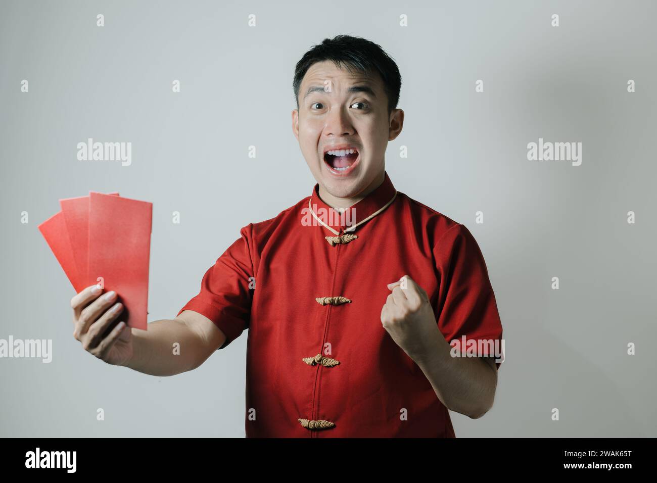 Visage heureux de l'homme asiatique portant Cheongsam ou tissu traditionnel chinois tout en tenant angpao ou cadeau monétaire rouge sur fond blanc. Gong Xi Fa Cai. Banque D'Images