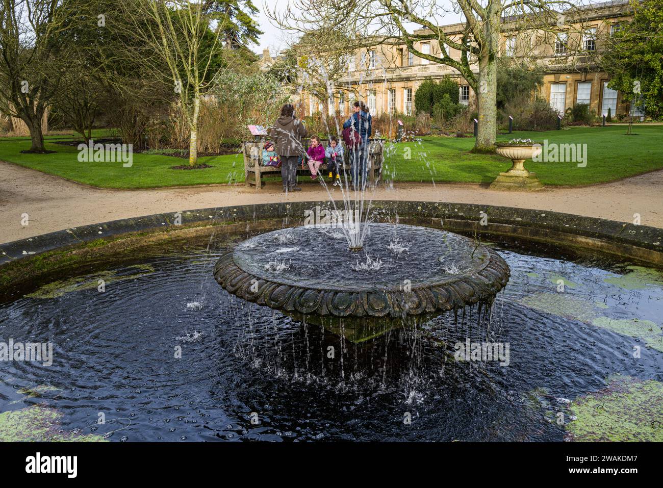 Des gens sur un banc à Oxford Botanic Gardens, Royaume-Uni, à moitié cachés par une fontaine Banque D'Images