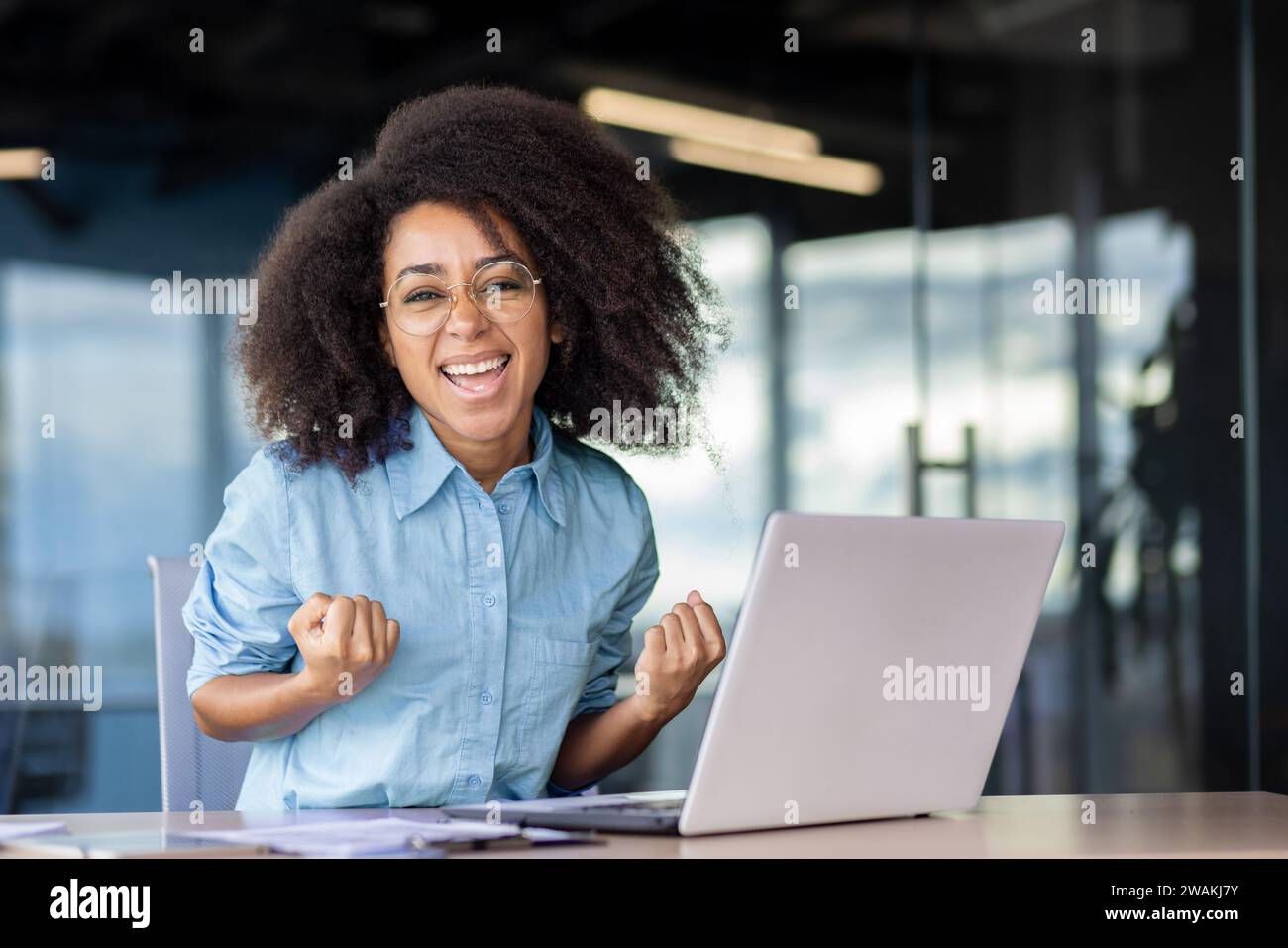 Portrait d'une jeune femme d'affaires heureuse et réussie assise dans le bureau devant l'ordinateur portable et regardant heureuse à la caméra, célébrant et Banque D'Images