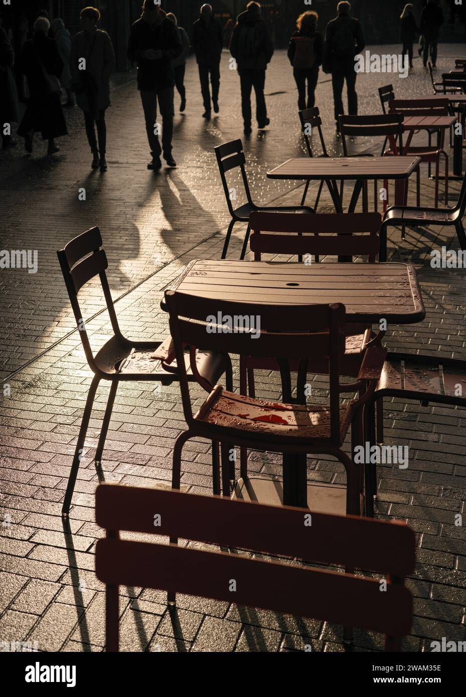 tables et chaises disposées dans la rue avec des piétons marchant Banque D'Images