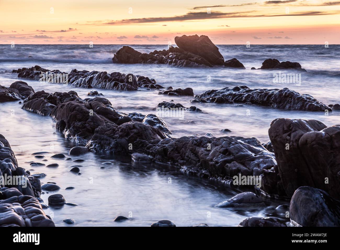 Rivage rocheux d'une côte au coucher du soleil, eau floue par exposition longue durée Banque D'Images