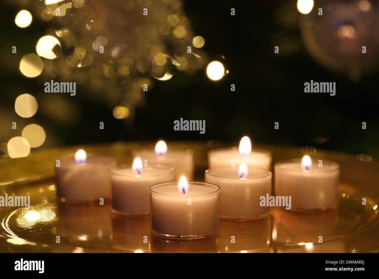 Gros plan d'un groupe de bougies chauffe-plat brûlantes sur une plaque dorée et sur fond sombre de Noël Banque D'Images