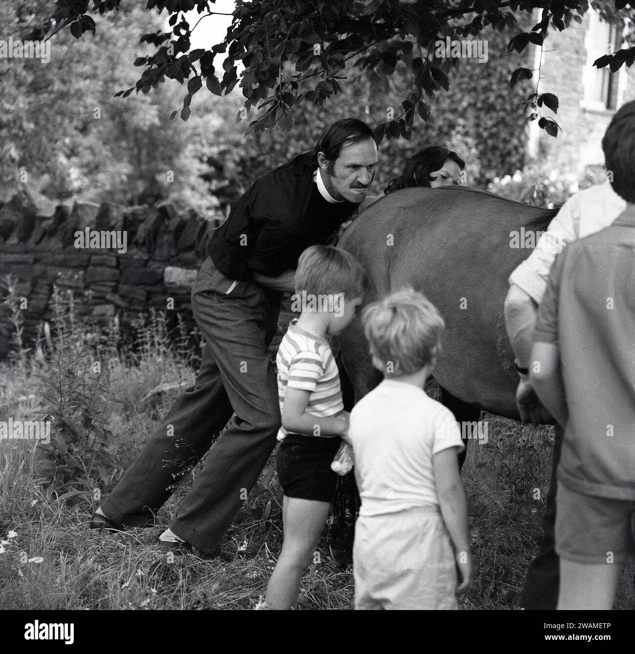 Années 1970, historique, estivale et extérieure dans un coin de champ, un vicaire aidant à pousser un cheval dans une remorque à une foire de vapeur, Angleterre, Royaume-Uni. Banque D'Images