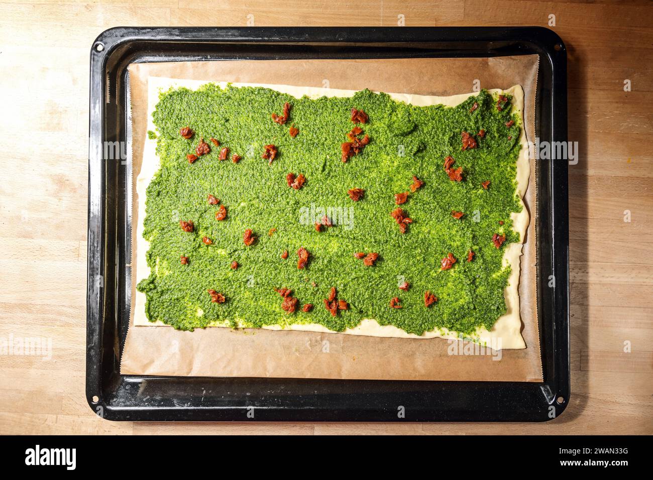 Pâte feuilletée avec pesto vert maison et tomates séchées sur une plaque de cuisson, préparer des amuse-gueules en Méditerranée pour une fête, vue grand angle f Banque D'Images