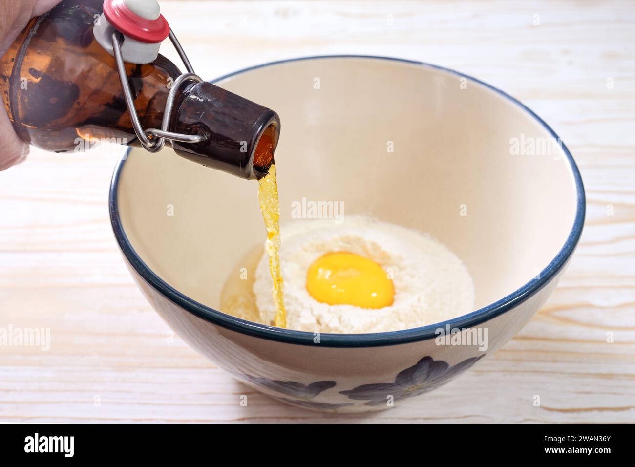 La bière est versée d'une bouteille dans un bol avec de la farine, de l'œuf et de l'huile pour faire une pâte à bière ou de la pâte pour couvrir les légumes ou le poisson pour la friture, sélectionnés Banque D'Images