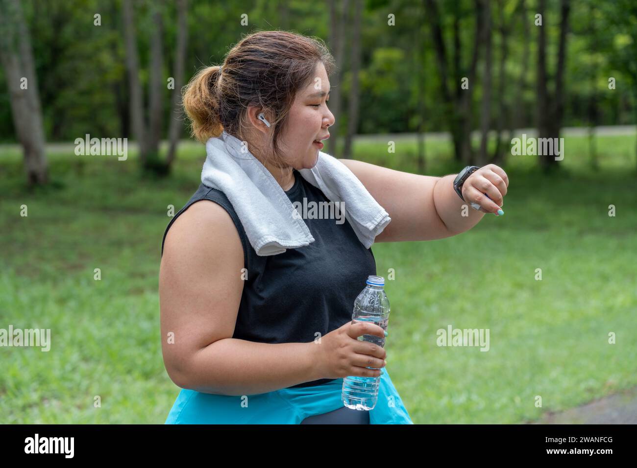 Jeune femme en surpoids vérifiant le résultat de sa course matinale sur sa montre intelligente tout en se tenant sur la piste de course d'un parc local Banque D'Images