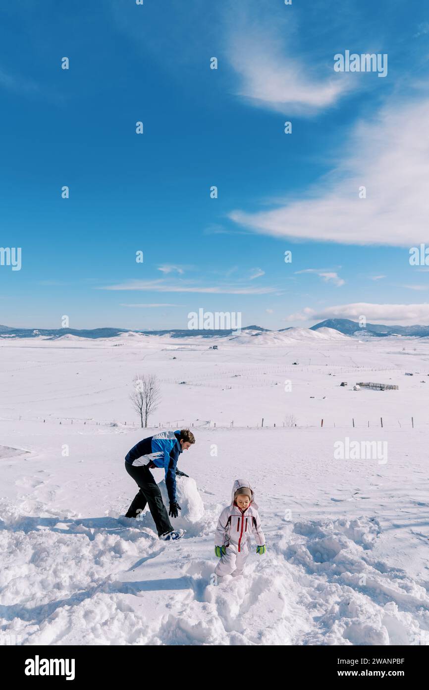 Petite fille et son père font un bonhomme de neige en roulant de grosses boules de neige sur la pelouse Banque D'Images