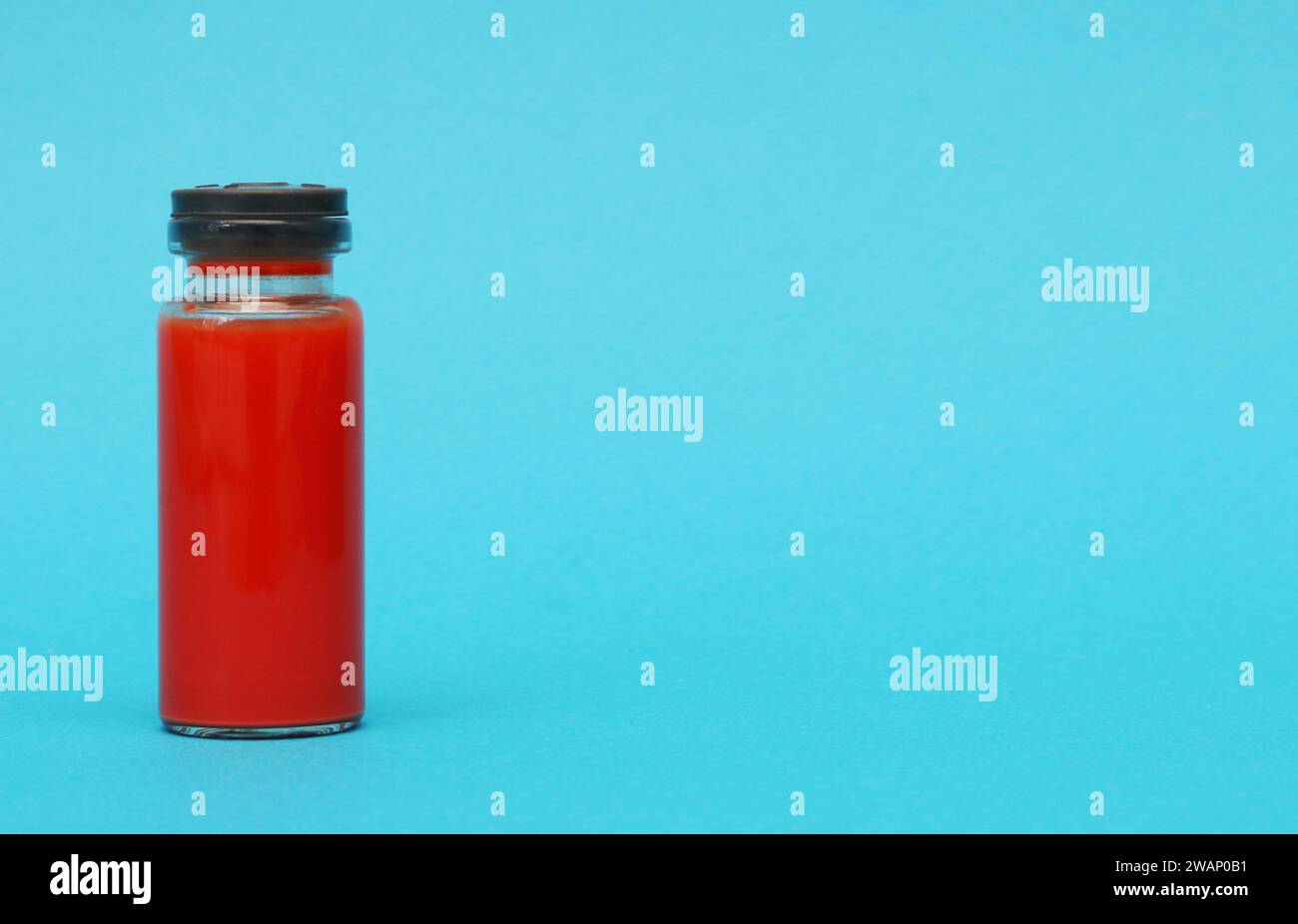 Ampoule avec un test sanguin. Bouteille en verre avec du liquide rouge sur fond de papier bleu. Banque D'Images