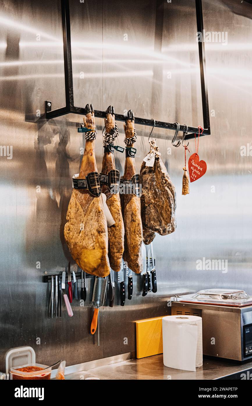 Jambons séchés suspendus dans une délicatessen espagnole. Des jambons traditionnels espagnols sont suspendus au-dessus d'un étalage de couteaux, dans une épicerie fine spécialisée. Varsovie Banque D'Images