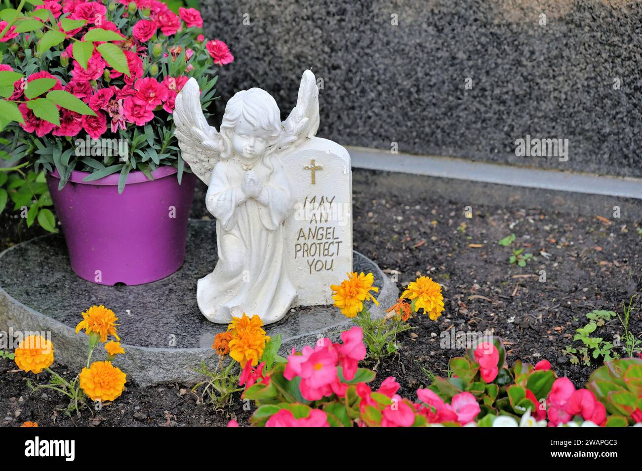 Ange grave avec inscription 'May an Angel Protect you' repose sur une dalle de granit entourée de fleurs Banque D'Images