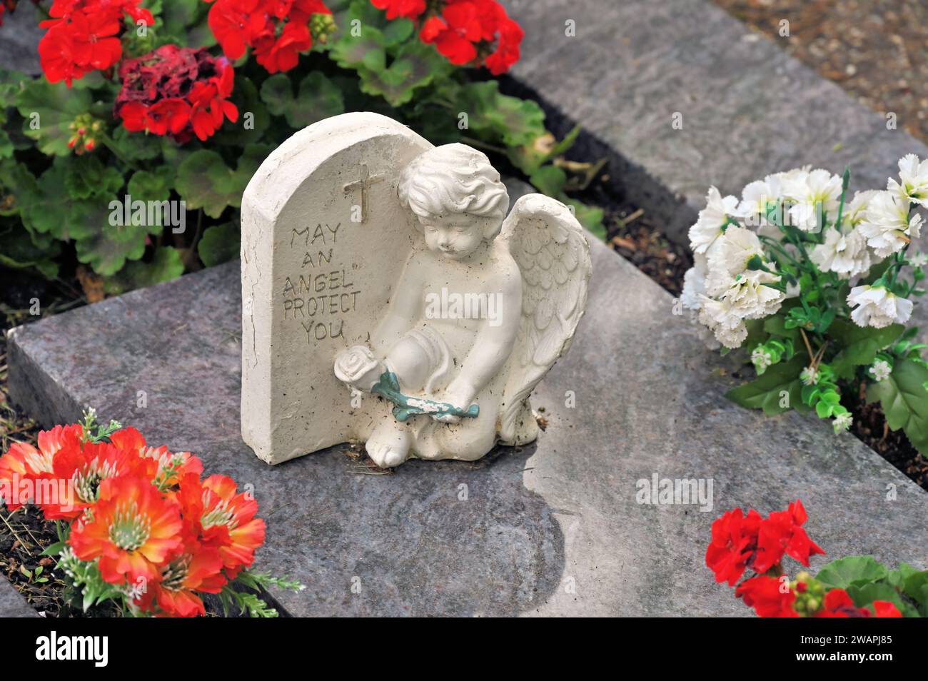 Ange grave avec inscription 'May an Angel Protect you' repose sur une dalle de granit entourée de fleurs Banque D'Images