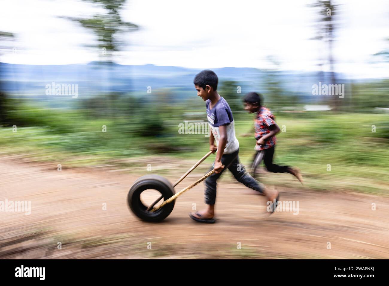 Garçon joue au cerceau et bâton avec un pneu dans une colline au Sri Lanka, panoramique photo. Décembre 2023. copyright caroljmoir/ Alamy Banque D'Images