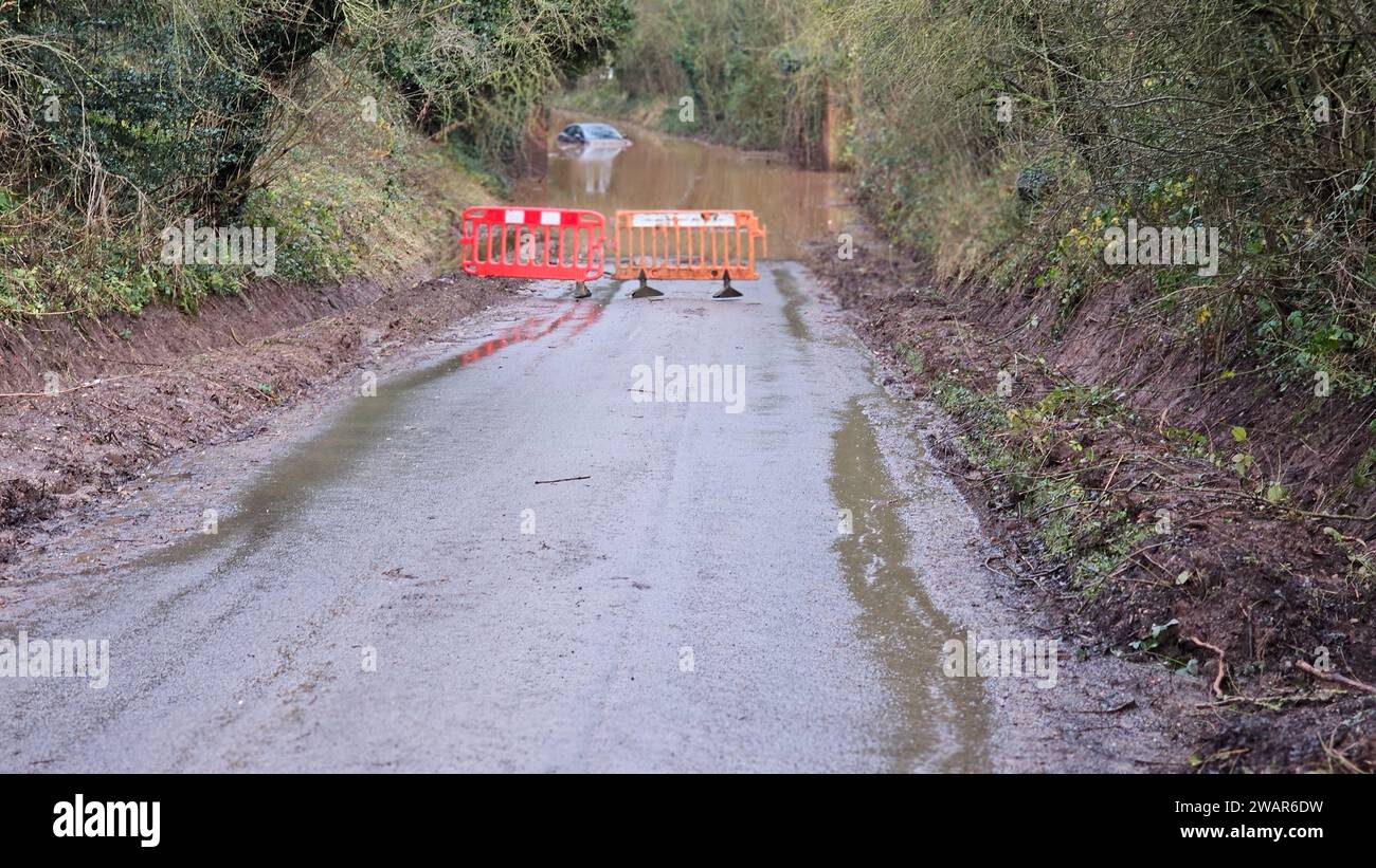 Une route rurale bloquée par une barrière remplie d'eau et des cônes de signalisation orange, soulignant l'absence de mouvement dans un cadre par ailleurs paisible Banque D'Images