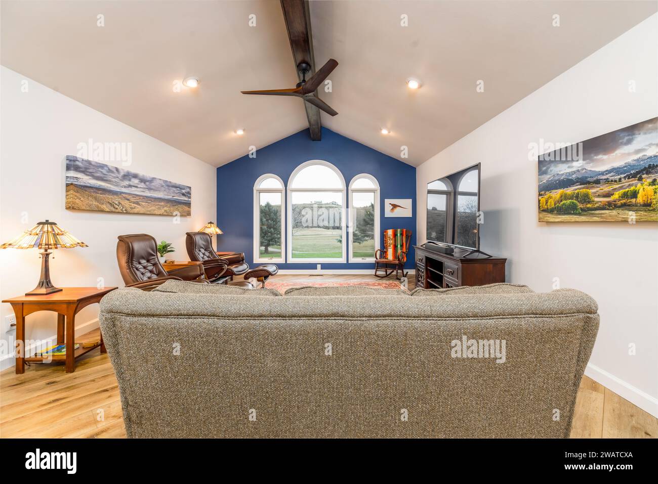 Un salon moderne confortable avec un canapé gris confortable, un ventilateur suspendu et une impression murale d'art d'une maison Banque D'Images