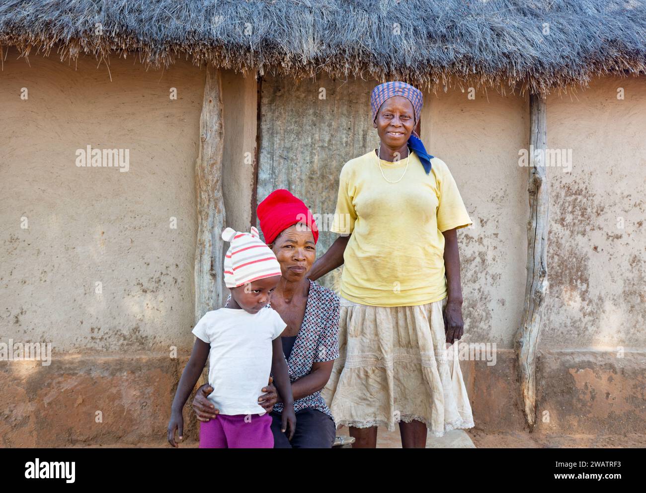 village famille africaine trois générations , debout dans la cour jour, devant la cabane de chaume Banque D'Images